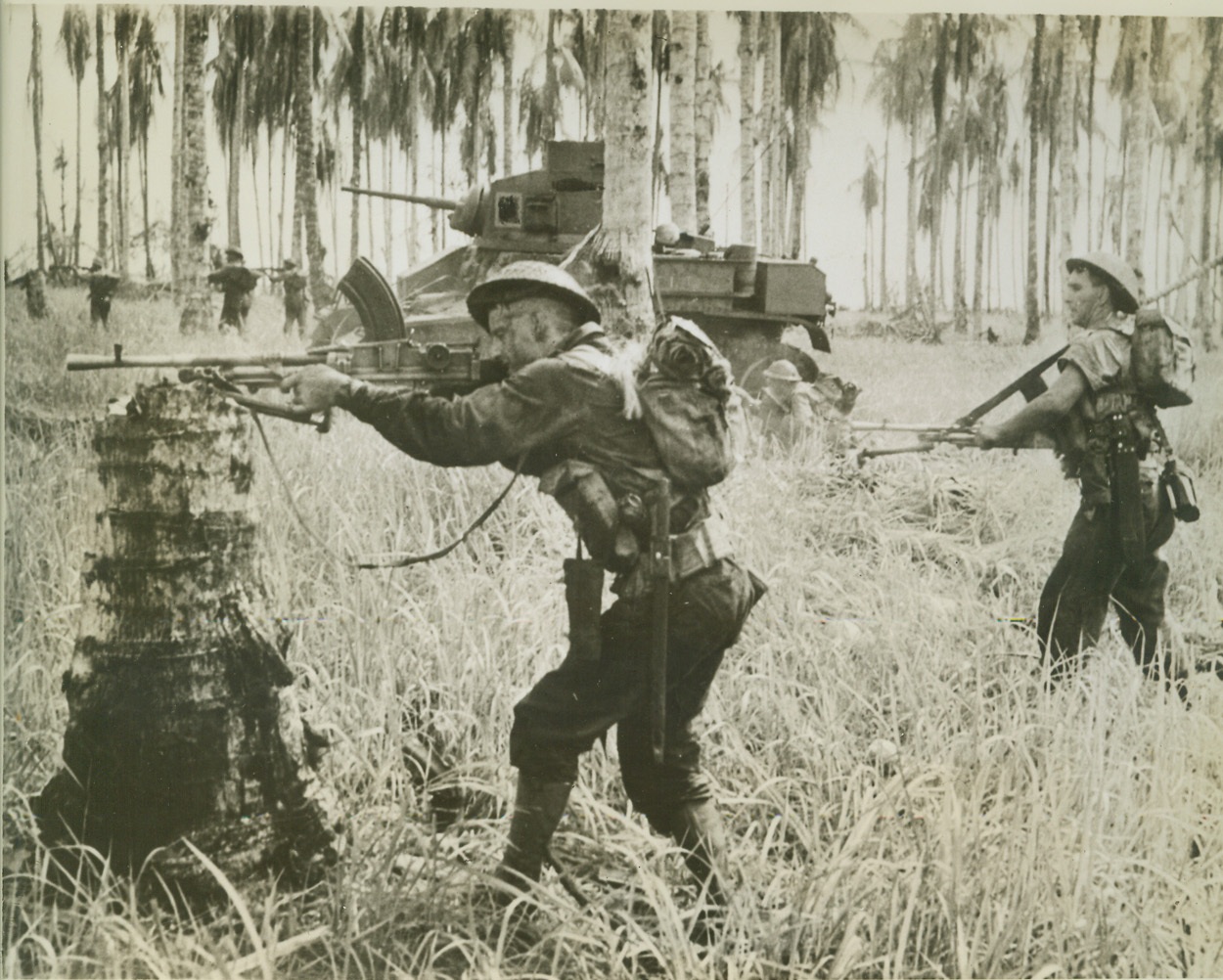 Aussies Stump Japs at Buna, 2/8/1943. New Guinea – A line of Australian troops beside a tank are firing on 25 Japs fleeing from a wrecked pillbox 150 yards away. One of the soldiers rests his gun on a tree stump to get a steadier aim. This is one of the first pictures showing the final assault on Buna. The troops exterminated Jap pillbox positions before rolling into Buna. Credit: (ACME);