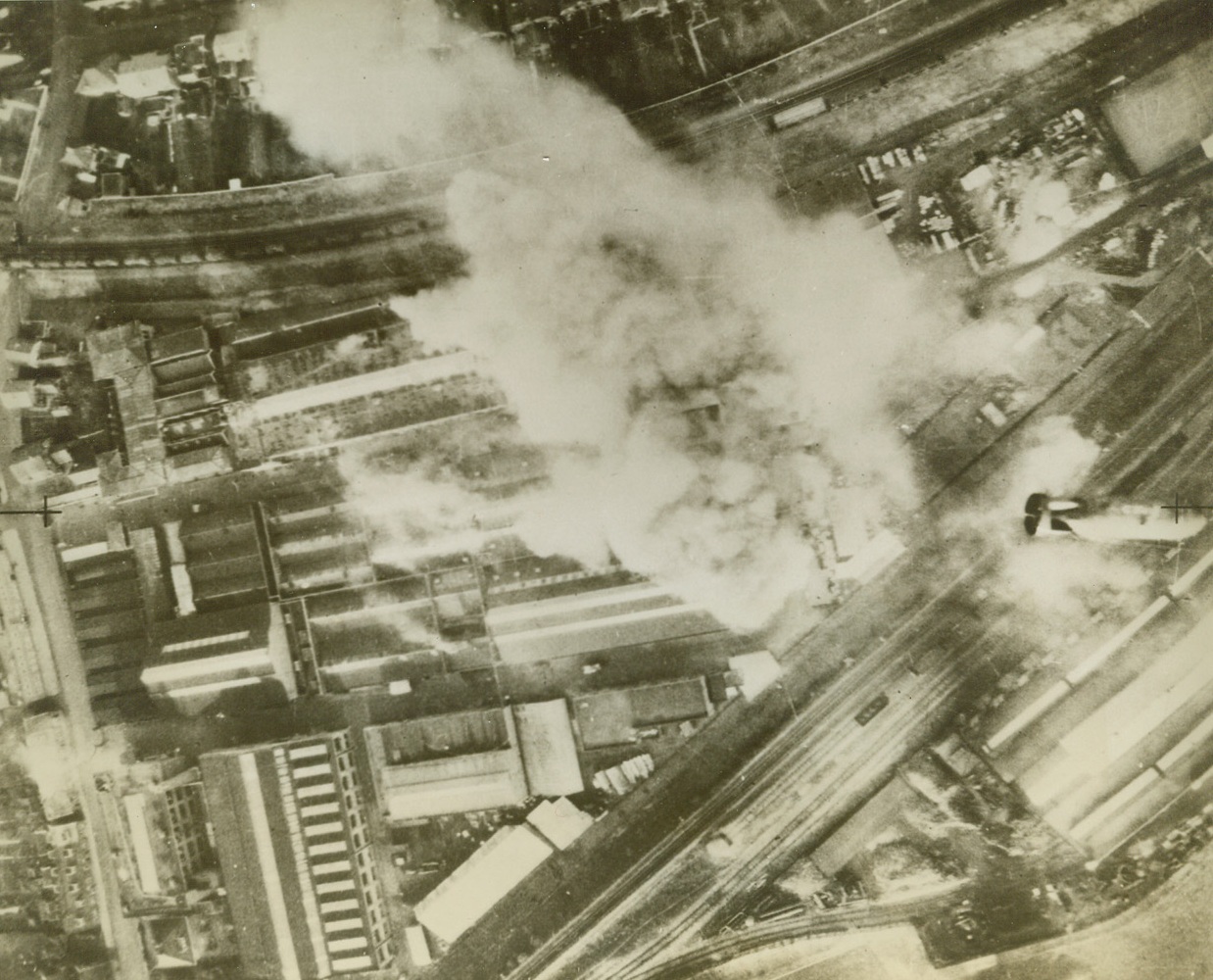 MOSQUITOS STING STORK, 2/5/1943. HENGELO, HOLLAND—As a bomb (lower center) from a Mosquito aircraft of the R.A.F. Bomber Command heads for the target, smoke from another direct hit pours from the south end of the Stork Engineering and Diesel Engine Works at Hengelo, Holland. This successful blow against Nazi U-boat production was struck in a daylight raid, January 20.  Credit Line (ACME);