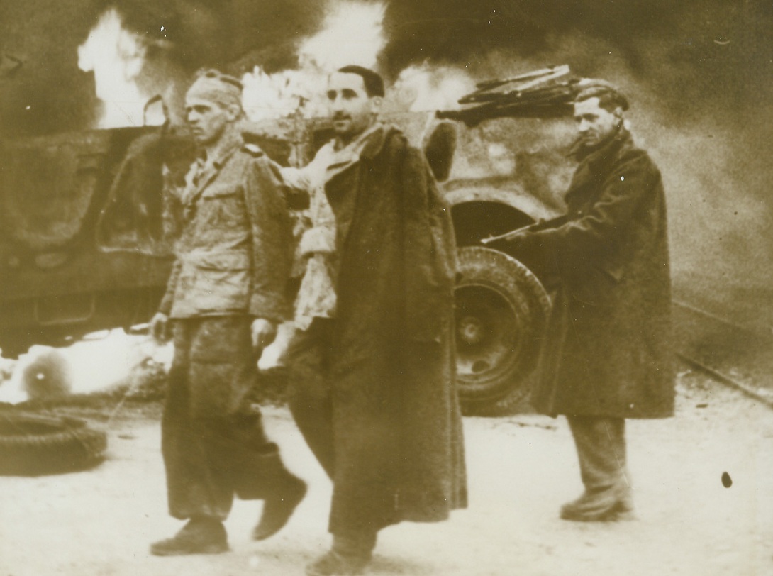 Allies Occupy Tunis, 5/19/1943. Tunis: - A British Tommy keeps his gun pointed at a pair of German prisoners whom he captured when Tunis fell to the allies.  The trio march past a Nazi vehicle that is still burning. Credit line (ACME);