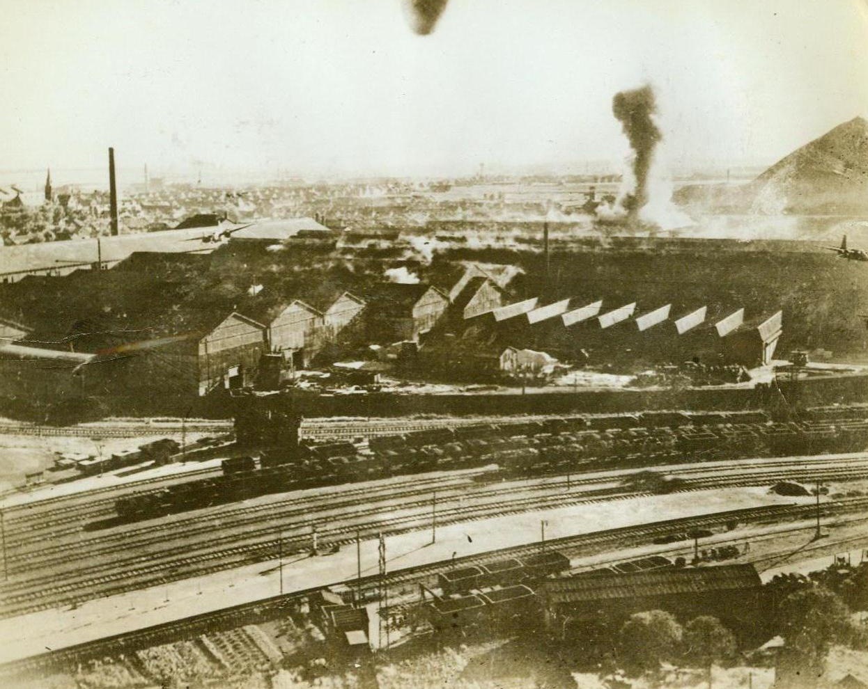 Boston Bombers In Action, 8/29/1943. Denain, France - With a smoke plume rising behind them as a bomb finds its mark, two Boston Bombers (to left and right of photo) of the RAF Fighter Command fly low over their objective, the important steel and armament works of the Societe Francaise De Construction Mecaniques and of the S.A. Des Hautes Forneaux Forges Et Acieres. The plants, which lie close together about five miles southwest of Valenciennes, were attacked from levels ranging from 50 to 1500 feet on August 16th. Although the industrial targets suffered heavy damage, destruction to residential property in the neighborhood was very light. Credit: ACME;