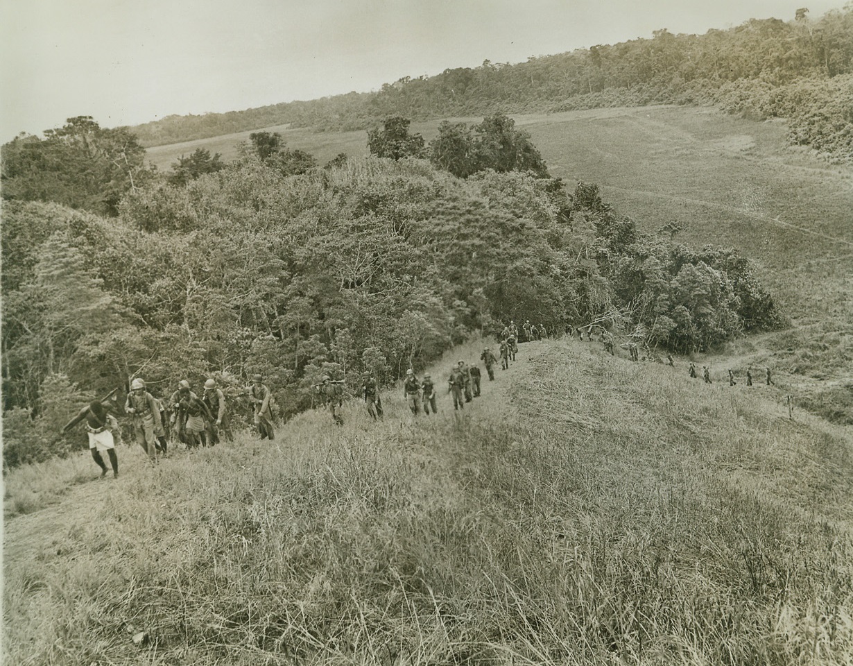 Safari on Guadalcanal, 1/16/1943. Guadalcanal – A Marine raider battalion – a specially trained group – marches over the rugged terrain of Guadalcanal.  They found the natives eager to help carry supplies and equipment.  One of the natives is serving as a guide. Credit (US Marine Corps photo from ACME);