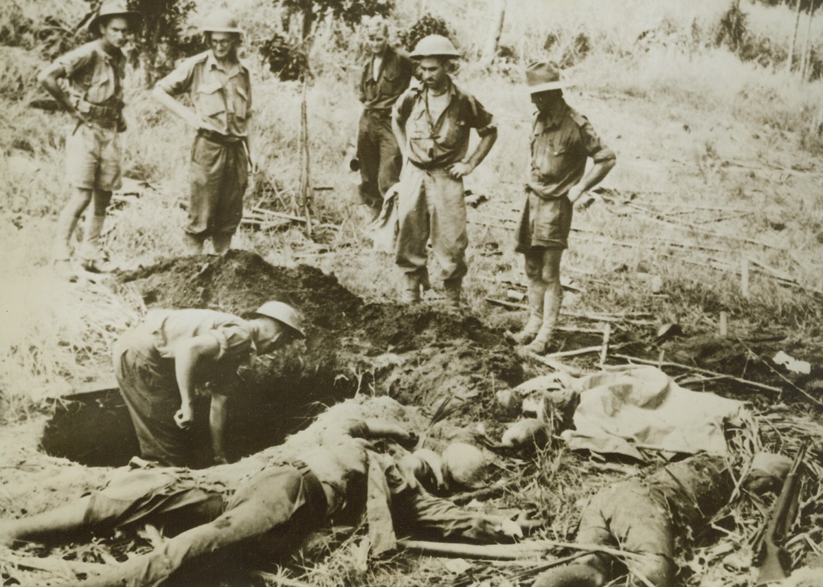 Victors Bury Vanquished, 1/8/1943. New Guinea – One Australian digs a grave for the two Japs (right), while the rest of the burial party stands by, ready to lower the dead Nipponese into the New Guinea earth they made the mistake of invading. This is a grim aftermath of the successful driving out of the enemy from the Easter part of Gona. Credit line (ACME);