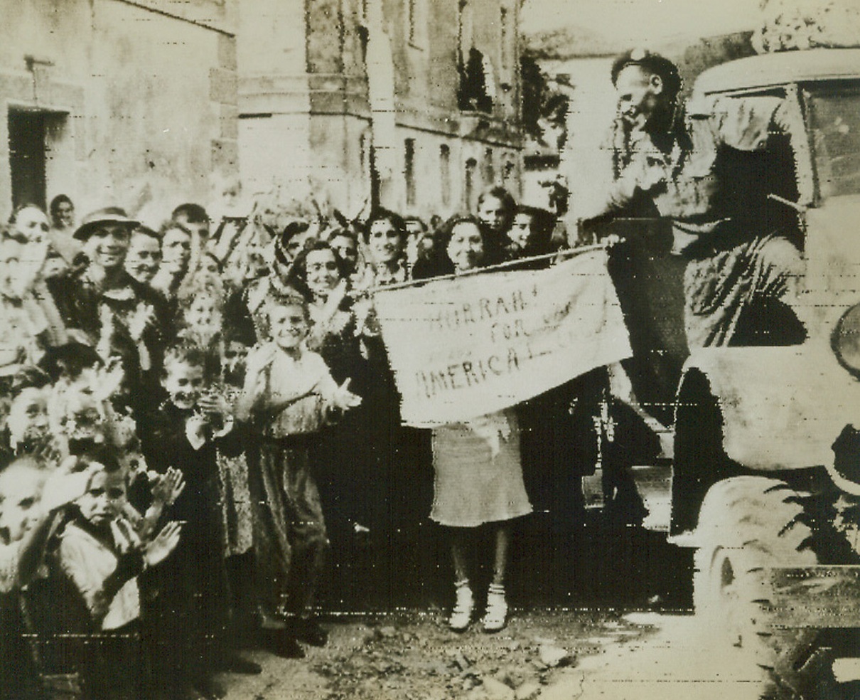 “WELCOME” SIGN OUT FOR THE ALLIES, 9/16/1943. An Italian girl holds a crudely-lettered sign bearing the legend, “Hurrah! For Canada, America, and England!” As Allied troops pass through Staletto in pursuit of the Germans. This photo was received in New York by radio today. Credit Line (OWI Radiophoto from ACME);