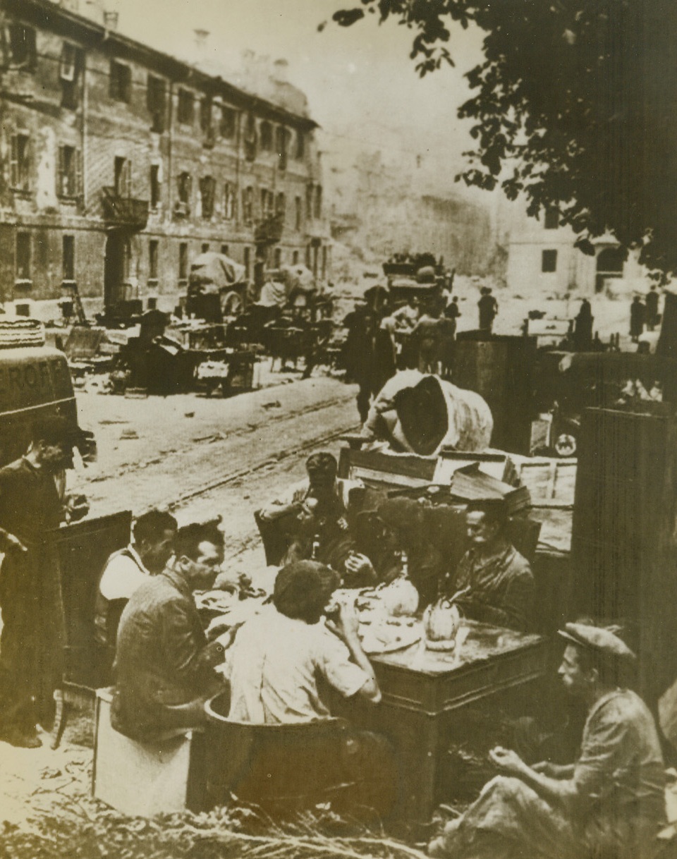 "Open House", 9/10/1943. Milan—After a heavy attack by allied bombers, inhabitants of Milan set up “open house in the streets of the industrial city. Furniture salvaged from bombed buildings, clutters the crowded street. Photo received through a neutral source. Credit: OWI Radiophoto via ACME;