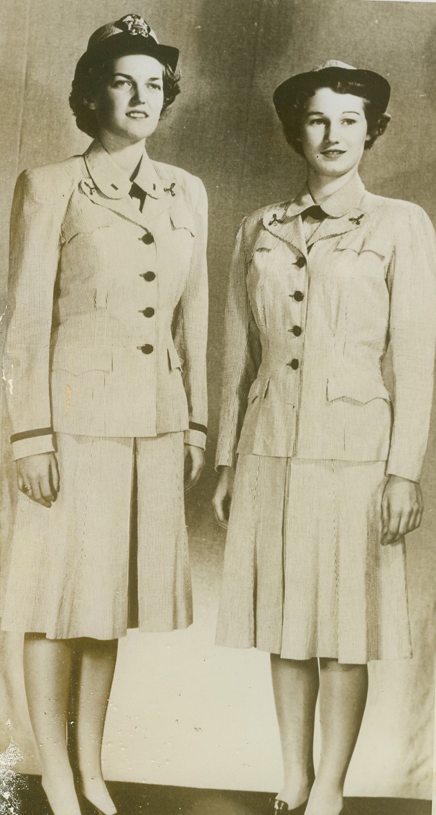 NEW SUMMER UNIFORM FOR WAVES, 10/1/1943. WASHINGTON, D.C.—Ensign Mary C. Broughton (left) of Washington, D.C., and Yeoman second class Marion Pearson of Cleveland, Ohio, both of whom are stationed in the Navy Dept. in Washington, model the new summer uniforms to be worn by members of the U.S. Navy Women’s Reserve. Gray and white striped seersucker, chosen to conform with the slate gray summer uniforms of Navy men, replaces the Navy cotton suit WAVES wore this summer. The removable hat cover is also of gray and white striped seersucker/Credit: Official U.S….;