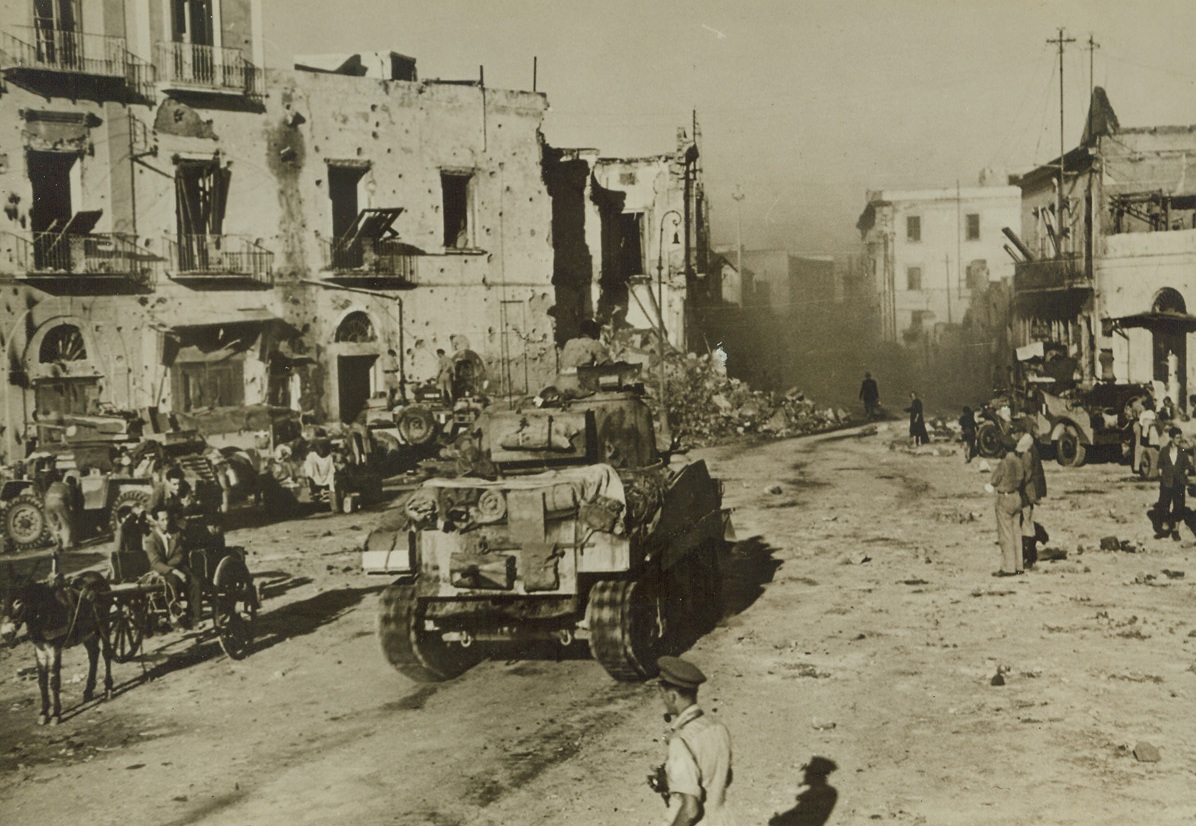The Town’s Main Square, 10/11/1943. ITALY—Dust that was once buildings fills the air in the square of Torre Annunziata, passed through by British Tanks on their way to Naples. Two civilians who were in the midst of furious warfare stoically sit in their donkey cart surrounded by mechanized equipment.  Credit: ACME.;