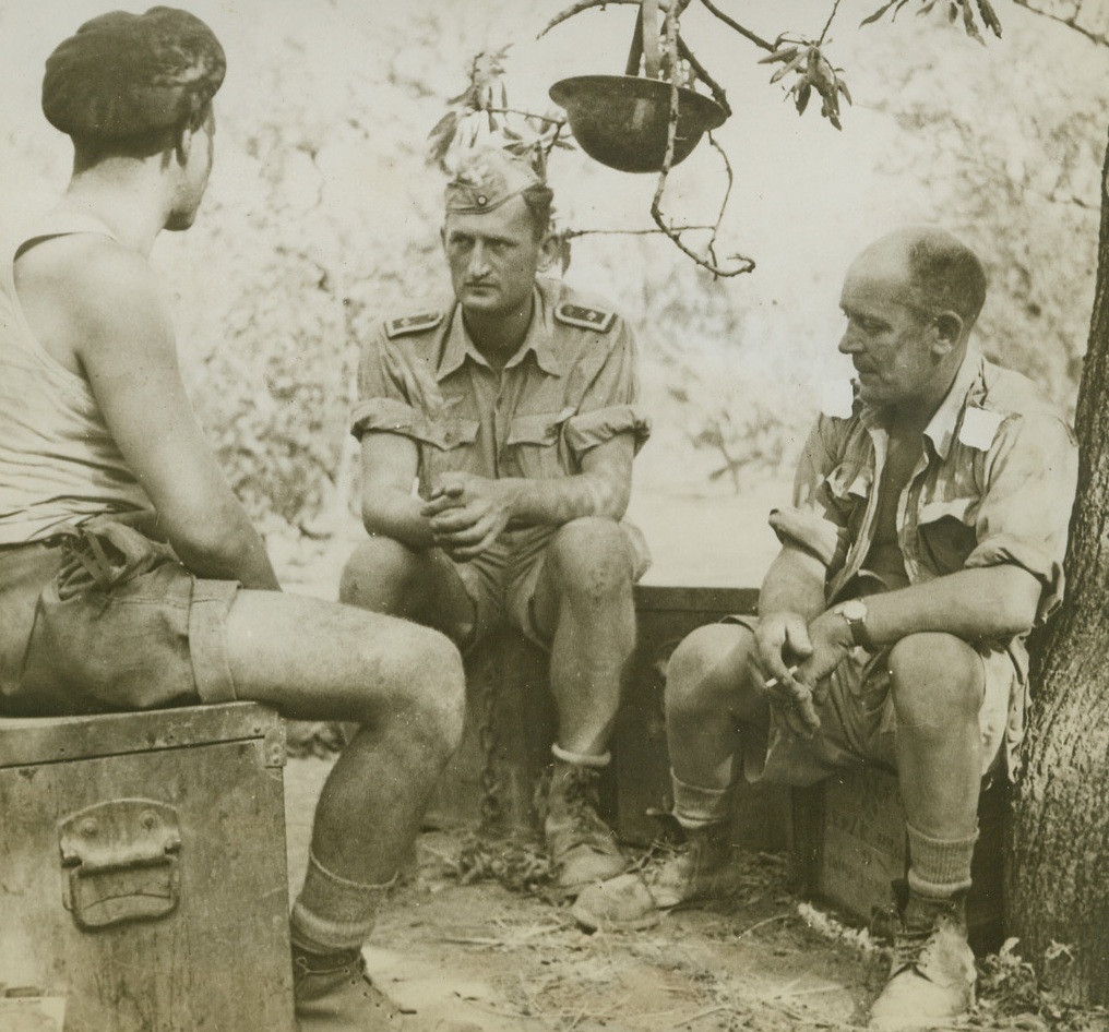 Two Points of View, 11/5/1943. ITALY—“Whatever made the Nazis think they could win this war, anyway,” might be the topic of conversation for this group: a British Corporal, driver, and German prisoner, who chat in Italy. They are Cpl. G.E. Sankey, of Birmingham, Dvr. H. Finamore, from Devon, and Sgt. Emile Ererich (center), of Vienna. The wing of this Allied plane, held in place by the flaps which will be lowered. Credit: ACME.;