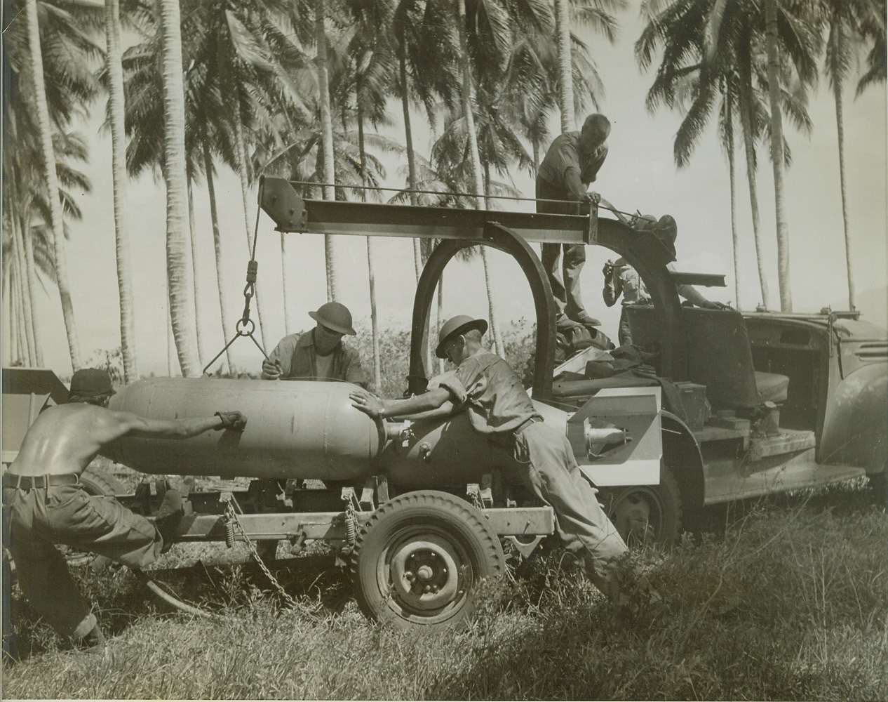 For Tojo -- Bad News from Guadalcanal, 10/14/1942. GUADALCANAL, SOLOMON ISLANDS -- With operational flights against Japanese ships and bases almost a daily affair, bomb loading crews of Marines on Guadalcanal airport are a busy lot. In this remarkable photo, bombs are being taken from "bomb gardens" concealed in palm trees, loaded on trailers and trundled onto the airport to be placed on U.S. Marine, Navy and Army bombers.  Credit (ACME);