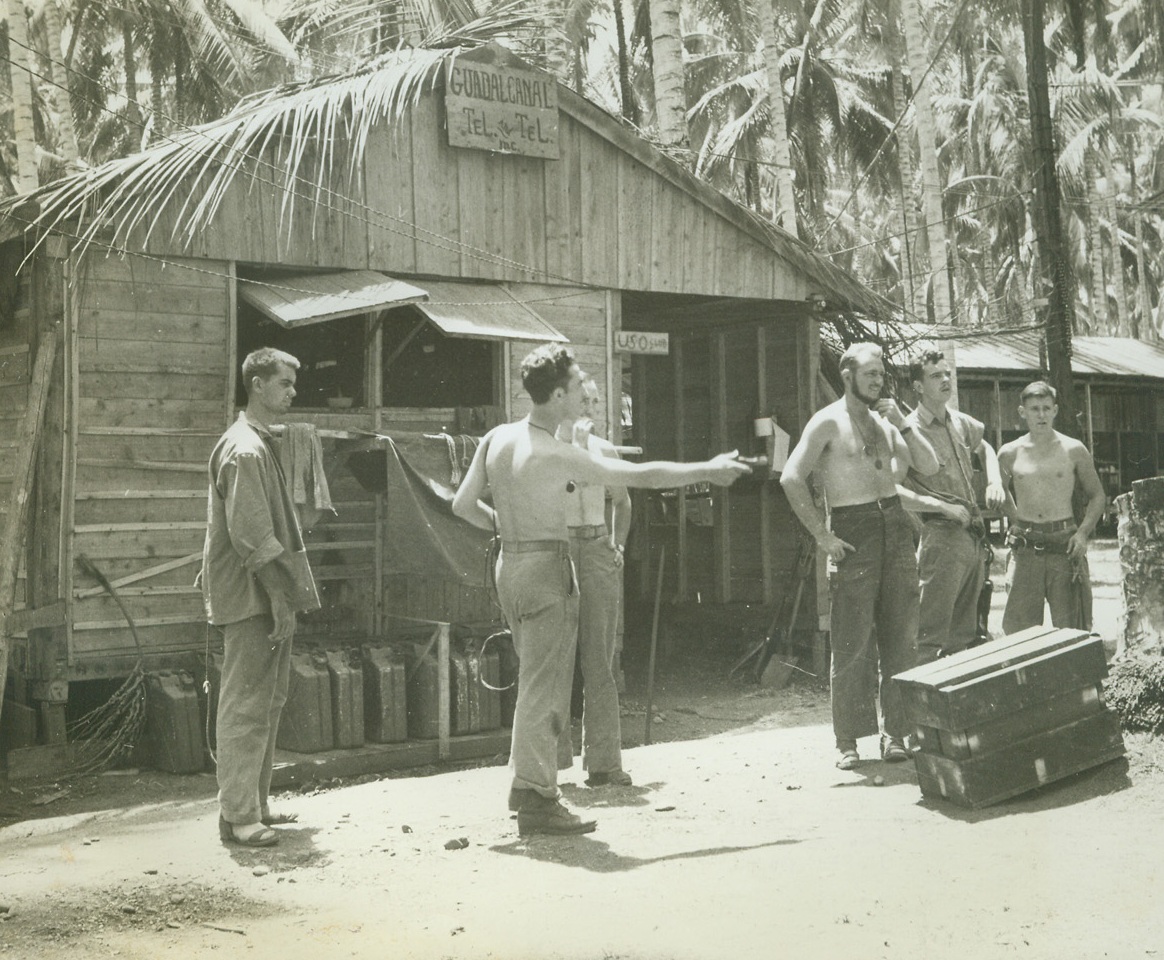 Telephone Building on Guadalcanal, 10/17/1942. Solomon Islands – Among the most imposing structures in almost any town is the telephone company building, and this is true of the U.S. Marines bas on Guadalcanal island, where anything more substantial than a tent is considered citified.  Here some of the “tel and tel” crew who are doing valuable work in maintaining communications for the Marines are shown outside of their headquarters. Credit Line (ACME);