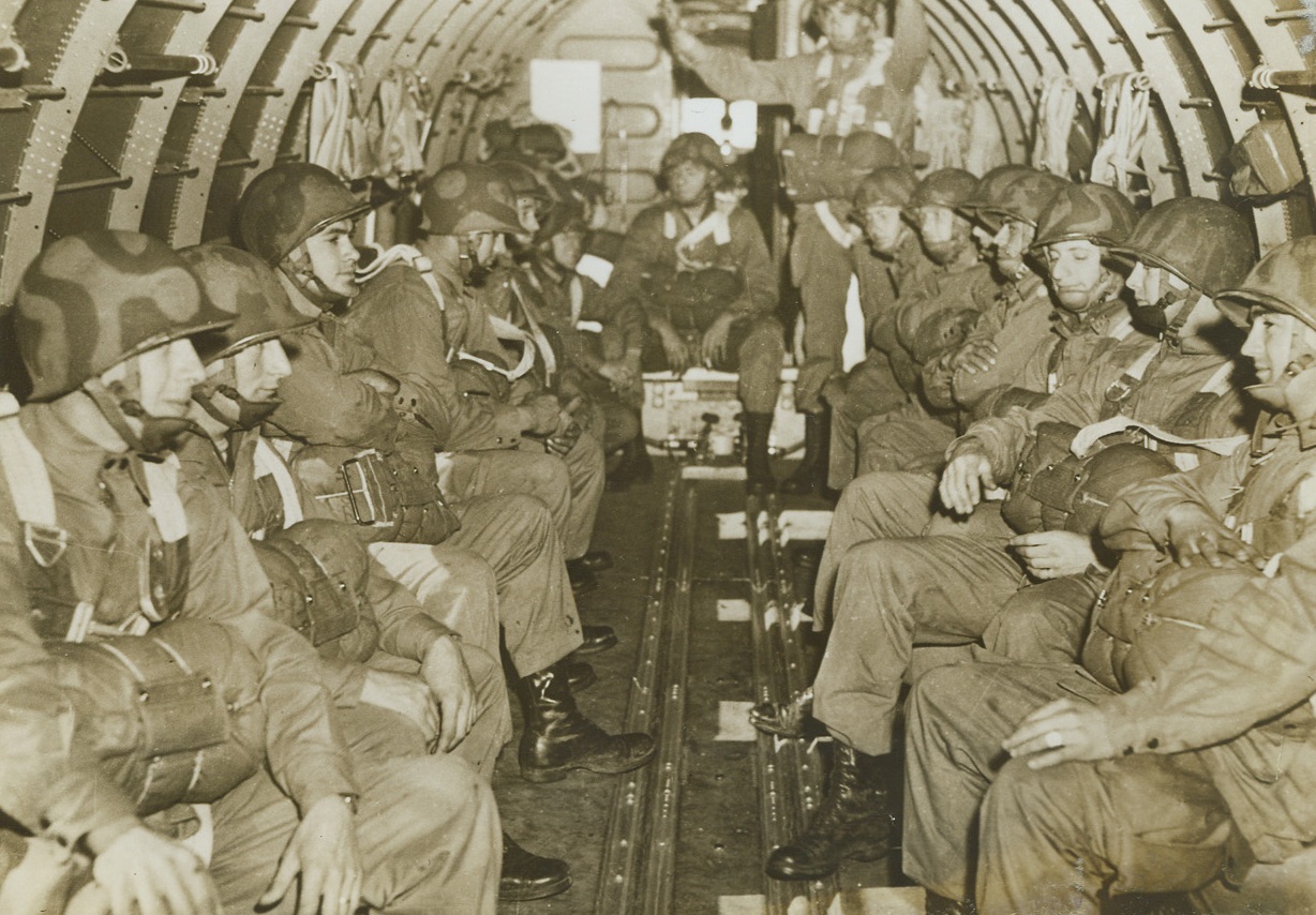 Before They Leap, 11/7/1942. North Ireland—Wearing their parachutes and camouflaged helmets, U.S. Paratroopers sit at ease along the sides of a big troop-carrying plane waiting for their cue to “hit the silk.” Photo was taken during training of American soldiers learning to be expert jumpers. Passed by censors. Credit: ACME.;