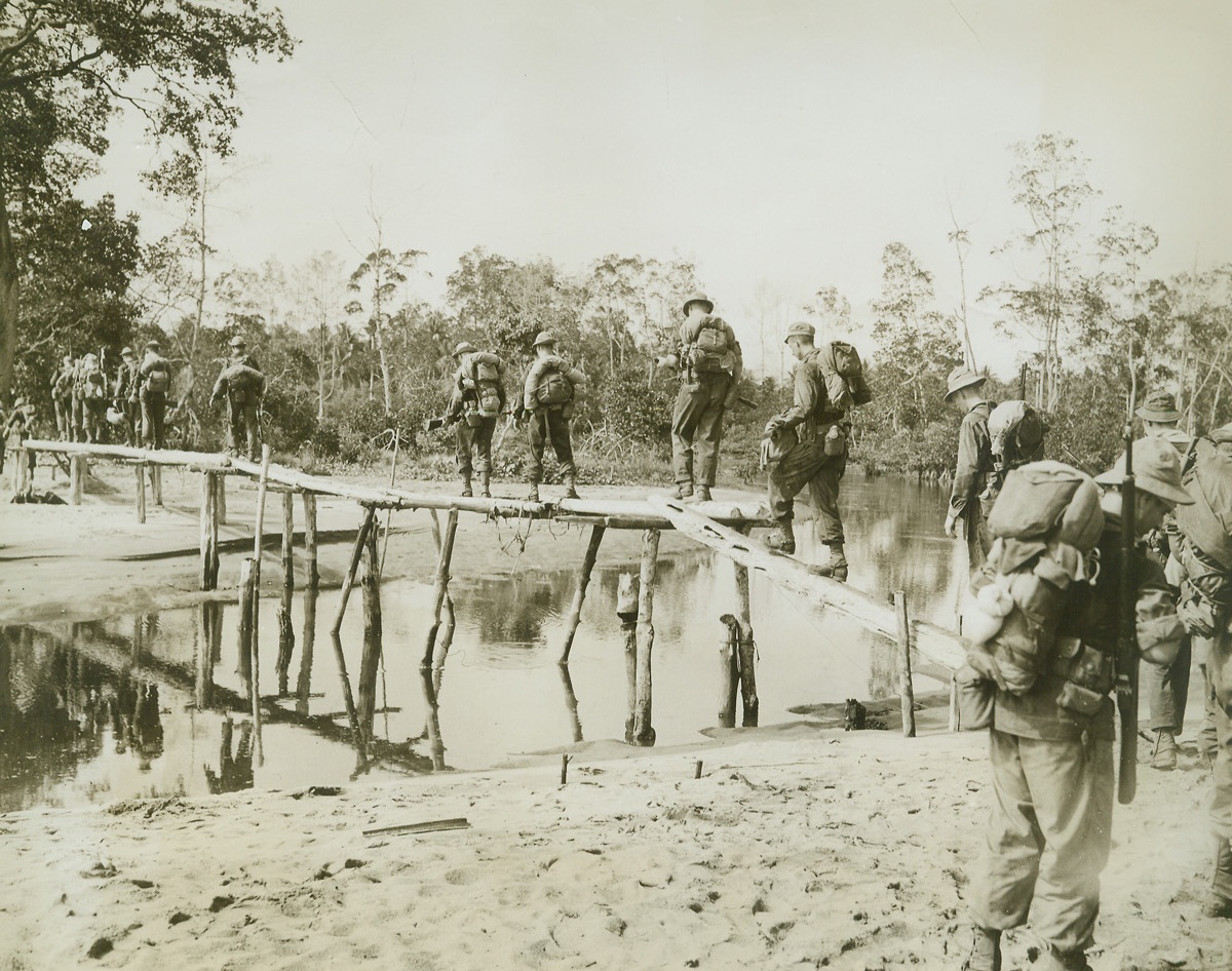 NEW GUINEA, TIGHT-ROPE WALK, 12/8/1942. SOMEWHERE IN NEW GUINEA—It’s balance not speed that counts as American infantry cross a small bridge to the edge of a jungle. Building their own bridges, constructing jeep roads out of nearby trees, and pushing through swamps, U.S. Doughboys moved to their present forward position in New Guinea.  Credit: ACME.;
