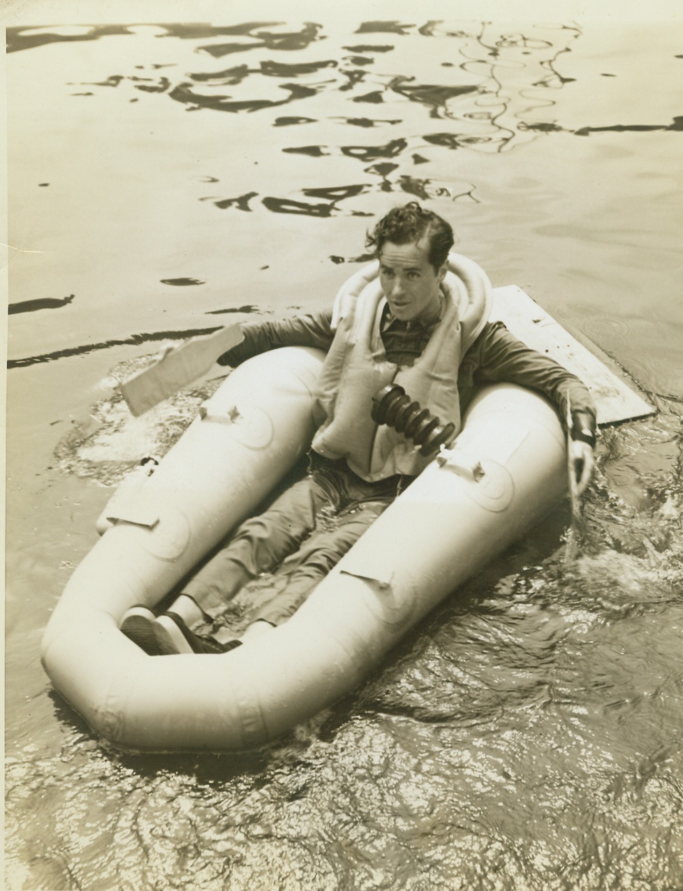 ONE-MAN PARACHUTE BOAT, 7/30/1942. NEW YORK – Ralph Douglas is shown in an ingenious new one-man parachute boat which the U.S. Rubber Company is producing for emergency use on single-seater fighter planes. It is attached to the pilot as a seat pack when he is in the plane. In a demonstration today, Douglas jumped into the East River with the packed boat and in less than ten seconds had it inflated. The two wire reinforced fabric paddles he is using to propel and steer the boat are among the eleven items of vital equipment in the pack, which weighs only twelve pounds. Credit: OWI Radiophoto from ACME;