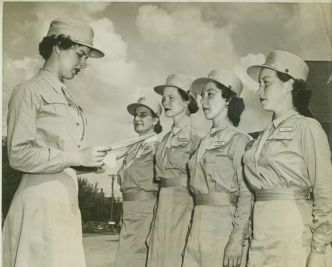WAAC HAS SERGEANTS TOO, 8/30/1942. FT. DES MOINES, IA. —Sgt. Wilma Stanton, Los Angeles, CA., first WAAC auxiliary (private) to be promoted to grade of Sergeant reads orders to members of her squad. Left to right: Helen Delvoski, Philadelphia, PA, Opal Aliff, Huntington, W. VA, Winifred Cioffi, Rutand, VT., Helen Hickman, Atlanta, GA. Credit: OWI Radiophoto from ACME;