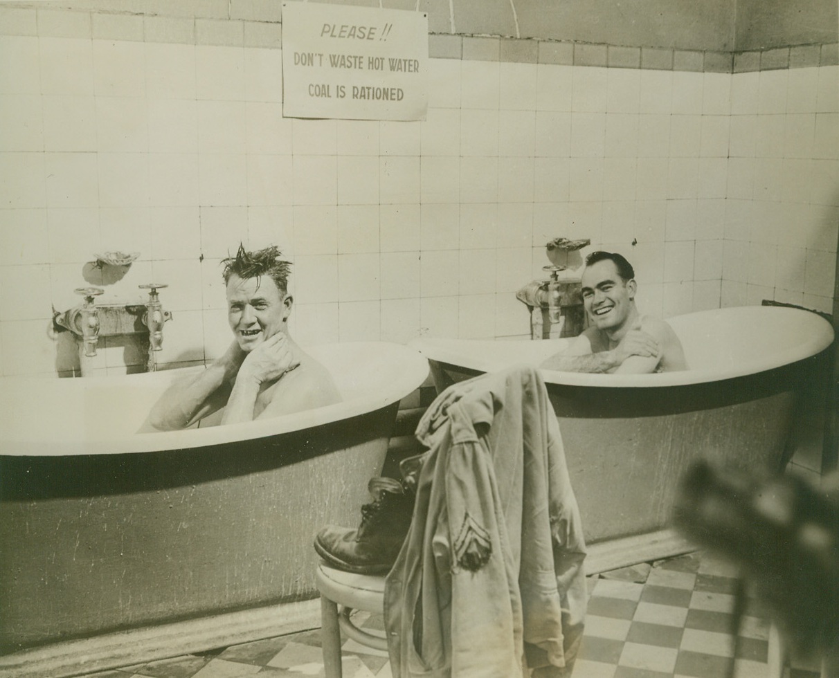 Two Men In Two Tubs, 12/15/1944. DIJON, FRANCE—CPL Manuel Holzenberg of Honey Grove Texas, and CPL George Clark of Arlington Virginia, enjoy a two-tub set up… (remaining text illegible);