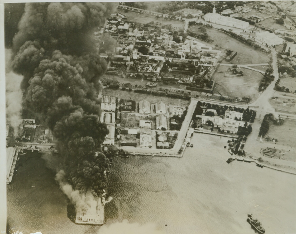 Yanks Uninvited Guests at Manila, 10/8/1944. MANILA -- Planes from V/Adm. Marc A. Mitscher's carrier task force paid a surprise visit to Manila and left calling cards in the form of these blazing docks. In the right foreground can be seen the swank Manila Hotel, with its gardens and yacht harbor. Municipal buildings, built by Filipinos before the Japs invaded the island, can be seen untouched in the background.  Credit (Official US Navy Photo From ACME);