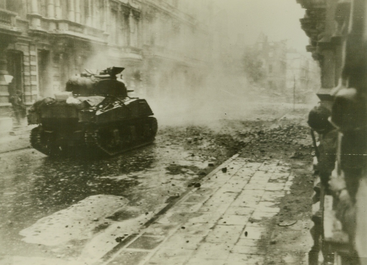 At Point Blank Range, 10/17/1944. As U.S. Infantrymen (right) peer cautiously down the street in Aachen, Germany, one of their tank destroyers fires at point blank range, at a target in the ruins of a building (right, background). Credit: (Army Radiotelephoto from ACME);