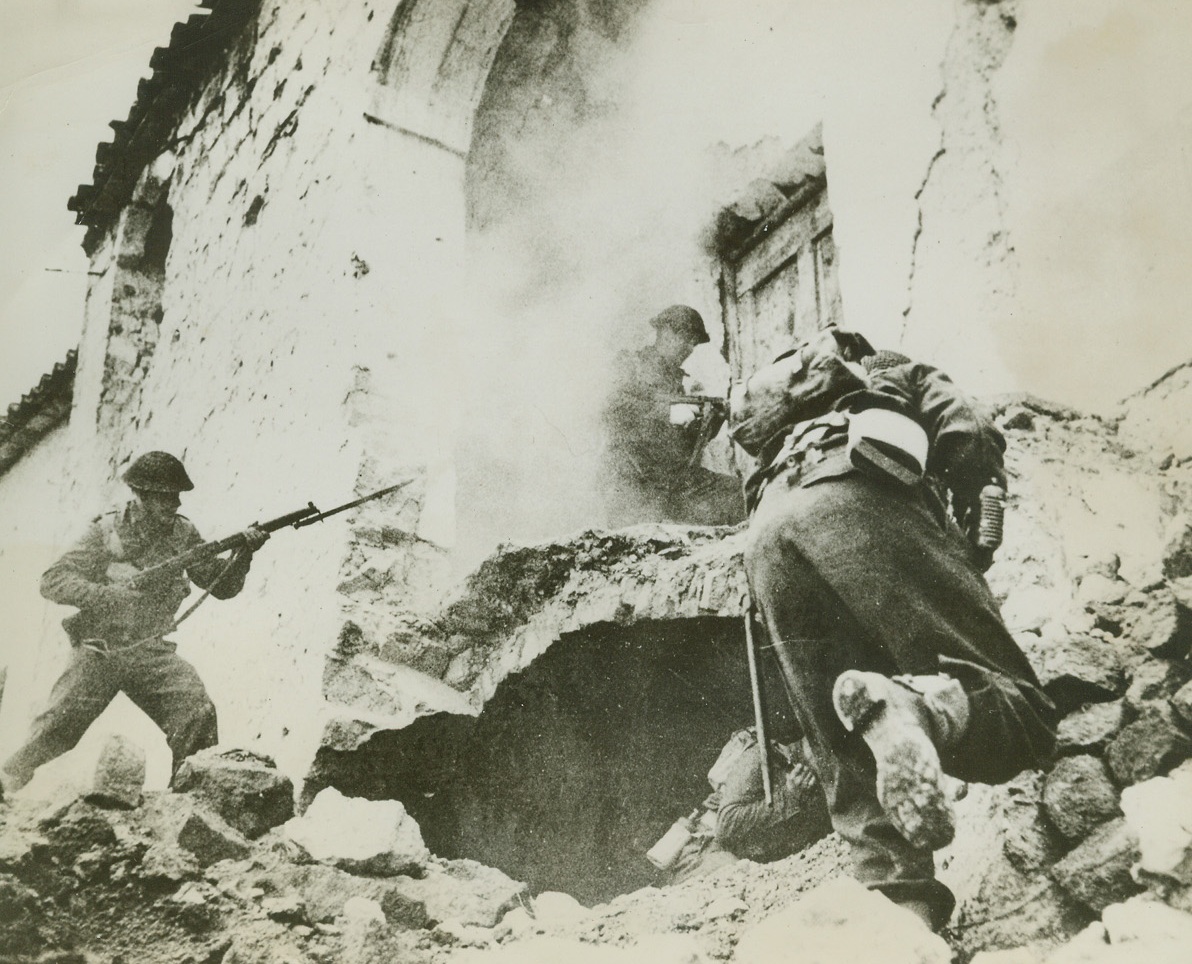 THROUGH BATTLE’S SMOKE, 4/9/1944. CASSINO—The smoke of battle still lingering on the scene, New Zealand infantrymen search a partially-demolished house in Cassino as they look for enemy snipers during the heavy fighting for possession of the German stronghold. Cassino has turned out to be the toughest single point in the entire Italy-Sicily campaign.Credit: Acme;