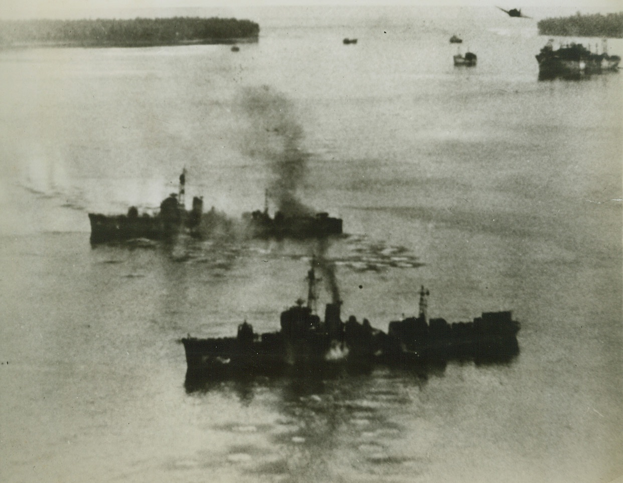 Merry Christmas, Dear Tojo, 4/7/1944. Kavieng, New Ireland – Delivering their Christmas gift to Tojo, Navy planes rained death and destruction on Jap cargo and warships at Kevieng, New Ireland, on Christmas day, 1943.  In the foreground two Jap escort vessels, the equivalent of our own destroyer escorts in size and weight, smoke from the attack.  In the background, a Grumman Hellcat swoops low to strafe a big cargo ship. Credit line (Official U.S. Navy photo from ACME);
