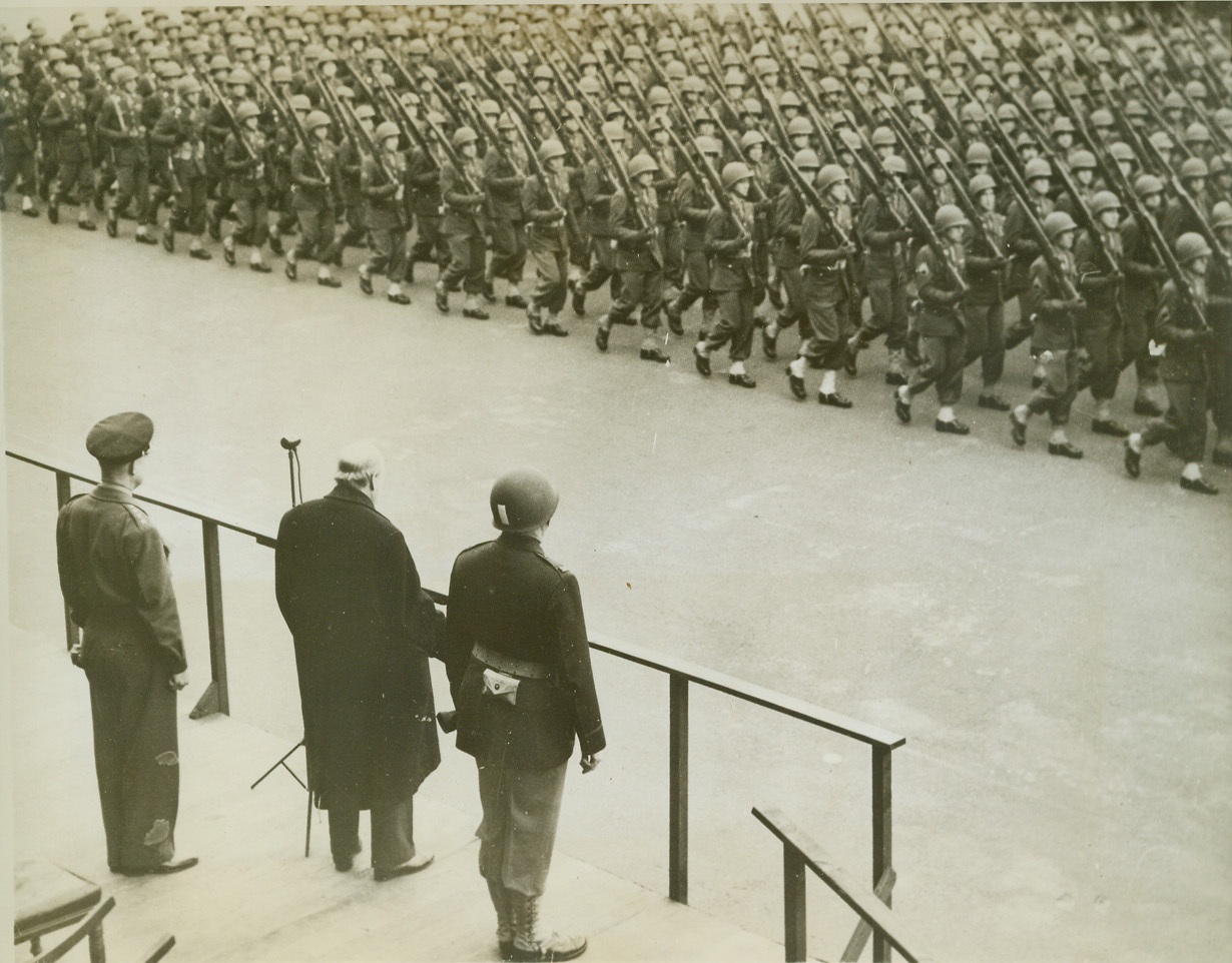 U.S. TROOPS PASS IN REVIEW, 4/1/1944. ENGLAND – Premier Winston Churchill watches American Infantry men from atop the reviewing stand as they march past in the famous Barpack Square. Mr. Churchill was accompanied by the Supreme Commander of the Allies, Gen. Dwight D. Eisenhower (left) on a recent review of the Second Front U.S. Forces in England. Credit: OWI Radiophoto from ACME;