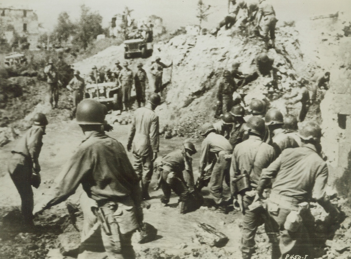 DAMAGED ROAD DIDN’T STOP ADVANCING TROOPS, 5/18/1944. ITALY—Retreating Germans blew up a bridge near Castellonorato in an attempt to impede the Allied advance on the town. Our troops, geared to the high tempo of the new Italian offensive, are shown filling in a road crossing next to the blown up bridge. Latest Italian announcement confirmed the German evacuation of Cassino, Nazi stronghold.Credit: US Army Radiotelephoto from Acme;