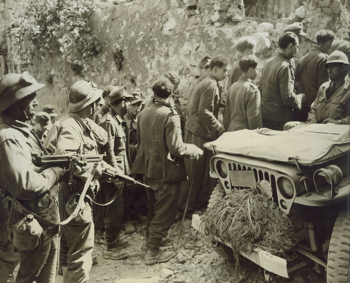 ALLIES SMASH GUSTAV LINE—FIRST PHOTOS, 5/18/1944. CASTLEFORTE, ITALY—This photo, one of the first originals to be received in the U.S. of the current smashing Allied offensive against the Germans in Italy, shows two American-equipped French soldiers of the Fifth Army, holding submachine guns ready for use (left), as they round up enemy soldiers in Castleforte after it had been taken by the Allies the second day of the attack. The Germans were left to defend the town “at all costs”, but were no proof against the fury of the Fifth Army advance. Today, five days after this photo was taken, the Allies have almost completely obliterated the Gustav line and are pressing strongly against the Hitler Line—last line of Nazi fortifications in Italy.Credit: Acme photo by Charles Seawood for the War Picture Pool;