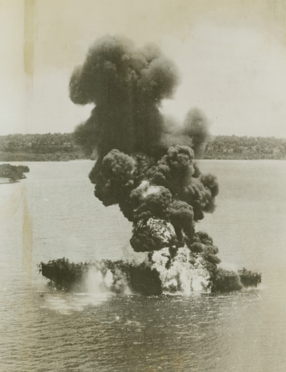 Jap Fuel Burns Beautifully, 5/20/1940. Timor – Smoke billowing skyward from the Pyre that has a Jap fuel boat, presents ample proof of Corp flyers marksmanship.  The barge was caught by allied planes in a bay at Timor in the South Pacific.  Flame and smoke indicate the cargo was probably oil.  Note the use of vegetation for camouflage – a vain gesture in this case. Credit (USAAF photo from ACME);