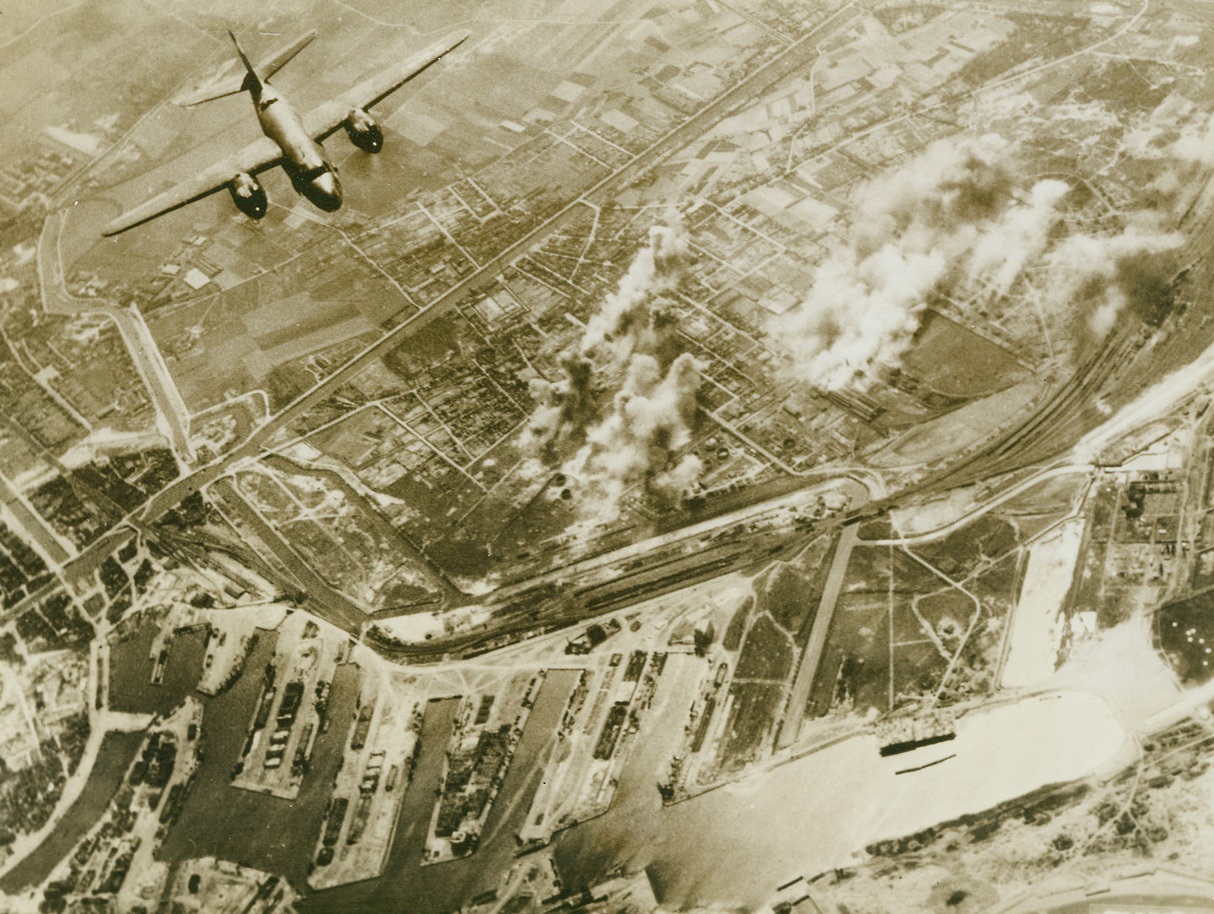 War Comes To Dunkirk Again, 5/16/1944. France – The bitter memory of Dunkirk is partially avenged as a 9th Air Force Marauder Bomber leaves a smoking target behind and heads for home after another sortie against Nazi military installations. The smoke from bomb bursts indicates hits on a railway and other objectives in Dunkirk. Credit: Official USAAF photo from ACME;