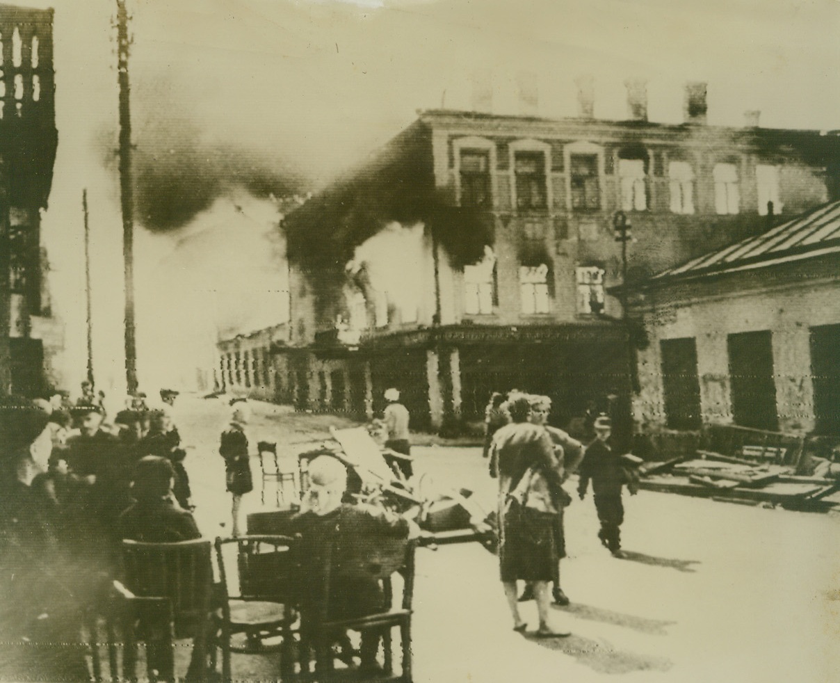 LIBERATED MINSK BURNS, 7/6/1944. MINSK—Residents of Minsk sit on salvaged furniture to watch homes, burned by the Nazis, go up in flames. Liberated by the rampaging Red Army, this former Nazi stronghold opens the gates on the road to Warsaw.Credit: Acme radiophoto;