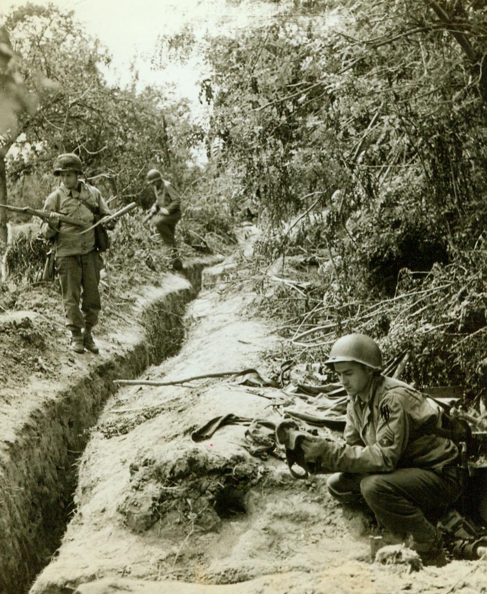 Captured Nazi Trench Near St. Lo, 7/20/1944. France -- Sgt. Thomas McMullen (foreground) of Maplewood, N.J., and Cpl. Leonard Redeyoff, Philadelphia, Pa., examine Nazi defenses in a trench hidden by a hedge in the St. Lo. sector of France. Trench was taken by Yank troops after bitter Nazi resistance had been quelled. Hedgerows around St. Lo provide perfect cover and makes it easy for the Germans to defend any given area. 7/20/44 (ACME);