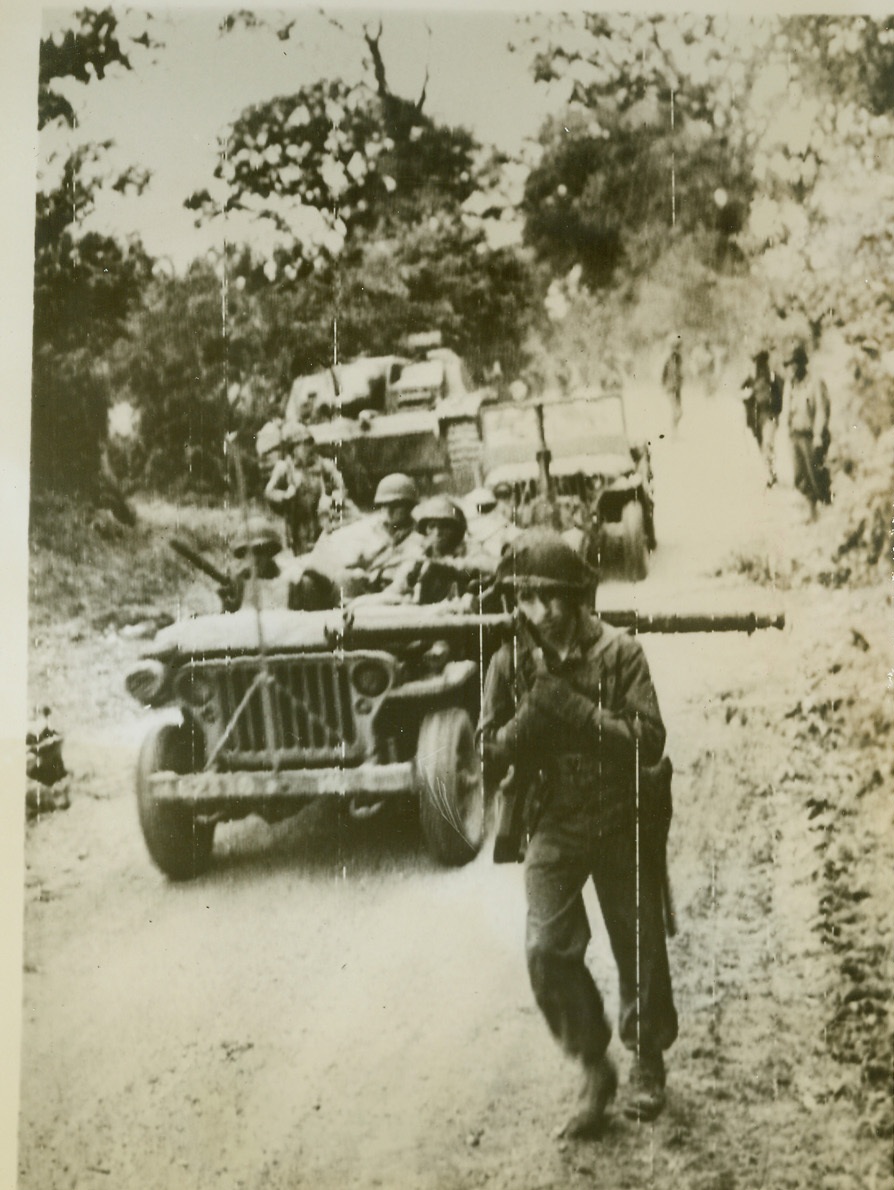Yanks Advance At St. Lo, 7/17/1944. St. Lo, France—After silencing the German M-4 tank seen standing at the side of the road in background, an infantry unit moves ahead in the St. Lo sector of the Normandy battlefront. The soldier walking in foreground carries a bazooka gun across his shoulders.  Credit: Signal Corps radiotelephoto from ACME;