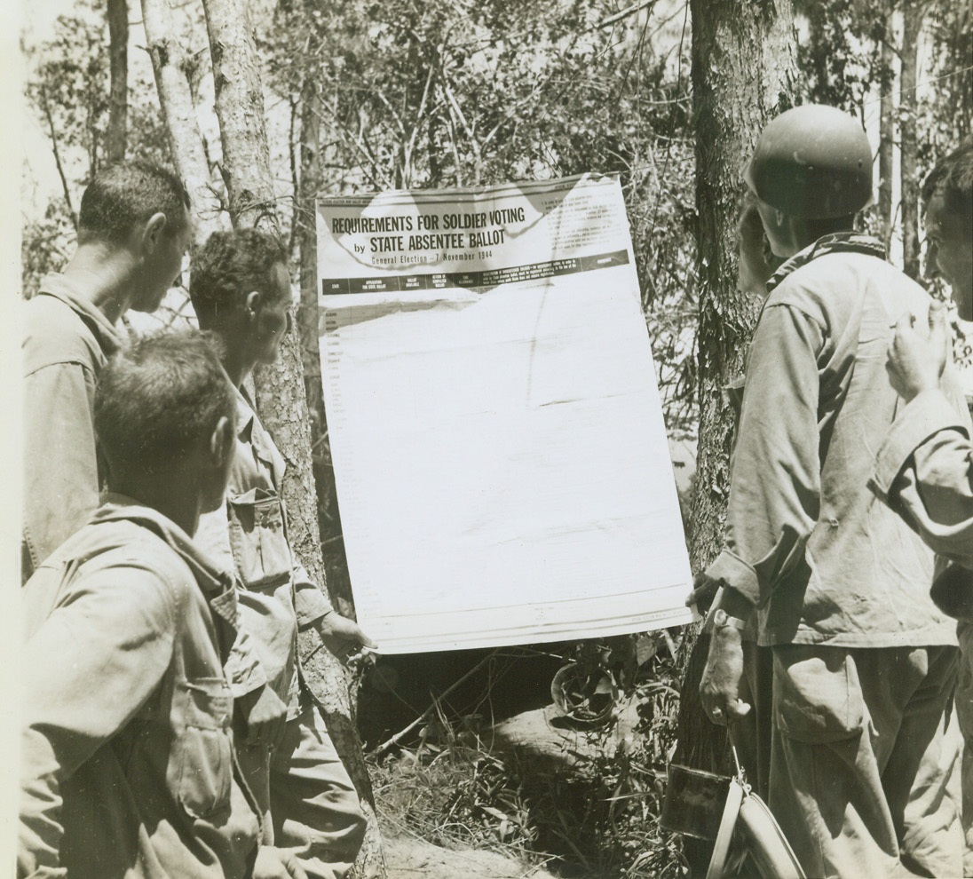 YANKS IN NEW GUINEA SEE ELECTION BALLOT, 8/11/1944. NEW GUINEA – Near the battle front down the Driniumor River, 16 miles east of Aitape on New Guinea, American soldiers take time out from war duties to read requirements for soldiers voting by state absentee ballot. Credit: OWI Radiophoto by Tom Shafer for ACME;