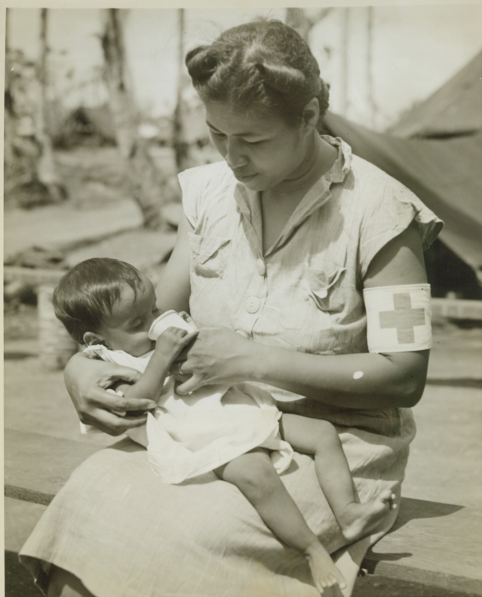 FIRST MILK FOR GUAM CHILD, 8/23/1944. GUAM – Nurse Maria S. Aguon gives this little 9-months-old baby its first taste of milk since birth at the civilian internment camp near Agana on the island of Guam. Many Chamorro mothers now in the camp, were fed so poorly under Japanese domination, that they had no breast milk for their babies. Credit: OWI Radiophoto by Stanley Troutman for ACME;