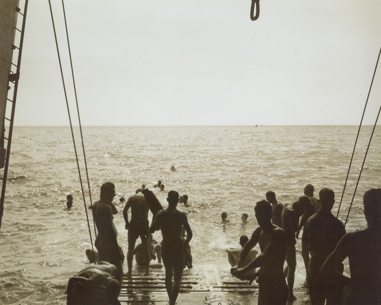 NO TIME FOR NERVOUSNESS, 8/22/1944. AT SEA—Veterans of the Italian and Sicilian campaigns and old timers at the business of invasion, infantrymen of the 45th Division relax before heading into the invasion of southern France. There’s no time for invasion jitters when the blue Mediterranean invites a fighter to take a swim. The boys dive off the [illegible] will soon bring them to the French coast. Credit: Acme photo by Sherman Montrose for the War Picture Pool;