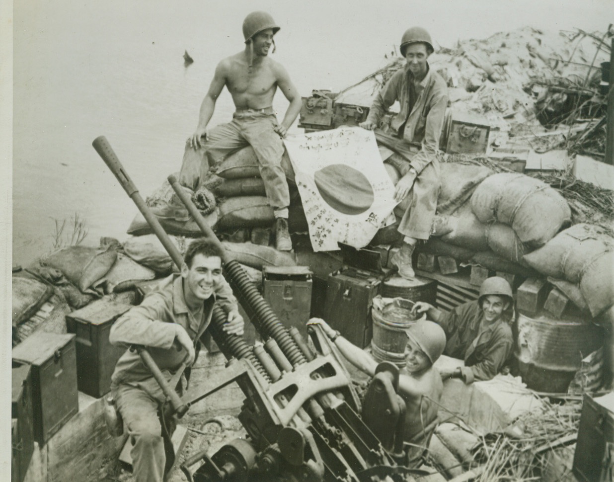 Jap Gun on Guam a Yank Prize, 8/2/1944. GUAM -- Useless now except as a memento of action gone by is this captured Jap gun taken during the American assault of Piti, Jap Naval station at Guam. In the gun pit are Sgt. Joe A. Grimes, Groesbeck, Tex. (rear, left) and Cpl. James W. Redding, (rear, right), Atlanta, Ga., examining a Jap flag, while (left to right, front) Pfc. Joe Woolsey, Jerseyville, Ill.; Pfc. Warren Jordan, Newark, N.J.; and Pfc. Joe Gilles, LaCrosse Wis., exhibit the gun. Credit- WP-(ACME);
