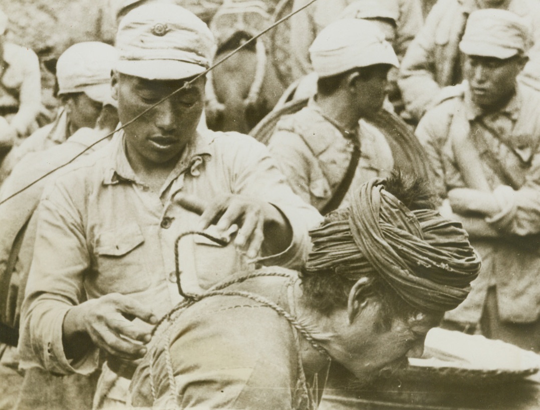 Up for Trial, 8/21/1944. China – Suspected of being a Japanese spy, this peasant is untrussed by a Chinese warrior at Division Headquarters on the Salween River front. Although he will be given a fair trial, the suspect will receive little sympathy from the Chinese if he is proven guilty. Jap spies are quickly disposed of by Chinese forces fighting to reopen the Burma road. Credit: Signal Corps photo from ACME;