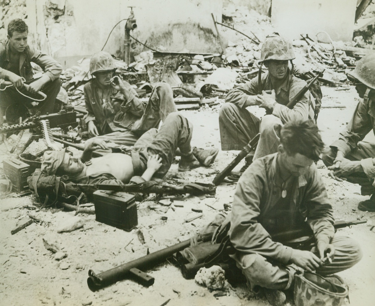 No Targets—Gun Crew Rests, 8/11/1944. AGANA, GUAM – When they ran out of Japs to shoot at on Agana, these gun crew members laid down their arms to relax for awhile, but they leave the cartridge belt in their gun—just in case. Left to right: Pfc. W. C. Dean, Meridian, Miss.; Pfc. R. A. Rouse, Cincinnati, Oh.; Pfc. E. J. Bernier (lying down), River Rouge, Michigan; and Cpl. T. L. McHugh, Cincinnati, Oh. Men in foreground and at extreme right are unidentified. All are of the Third Marine Division Credit: ACME;