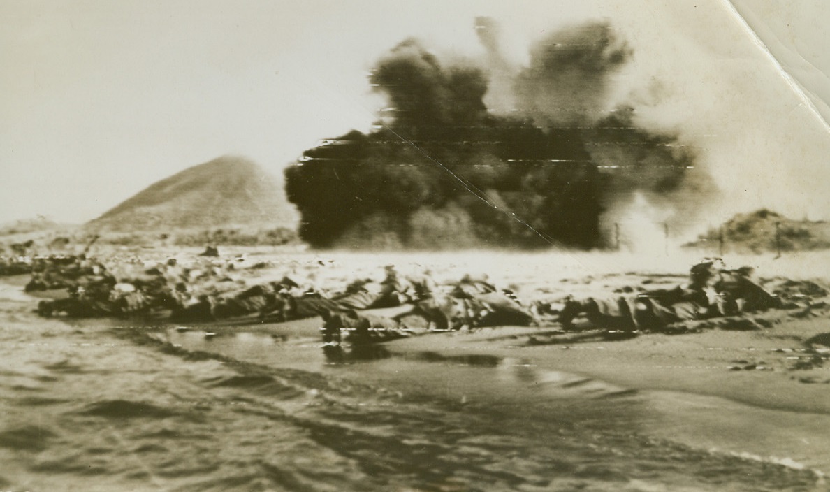 Invasion Practice for Yanks, 8/15/1944. U.S. Infantrymen lie flat on their faces in the sand, as their Bangalore torpedoes explode, shredding “enemy” barbed wire barriers along this “invasion” beach. This scene was, and is being reenacted along the shore of Southern France, as Allied forces pour ashore to establish the fourth front. Credit: Army radiotelephoto from ACME.;