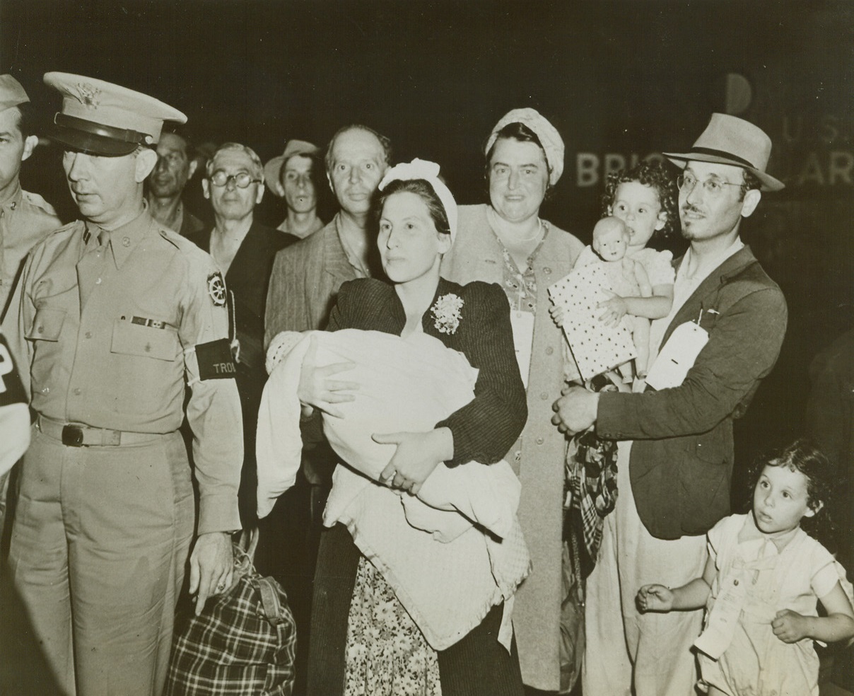 Free and Happy, 8/4/1944. Hoboken, New Jersey -- Headed for the train that is to carry them to Fort Ontario near Oswego, New York, is this family, part of almost 1,000 refugees from Italy who will remain in this country for the duration of the war. They are (left to right): Mrs. Netta Rothchild, holding her four-weeks old daughter Gratzia; and Mr. Isreal Rothchild, carrying his daughter Reneta as another daughter, Fanny, walks beside him. Credit: ACME;