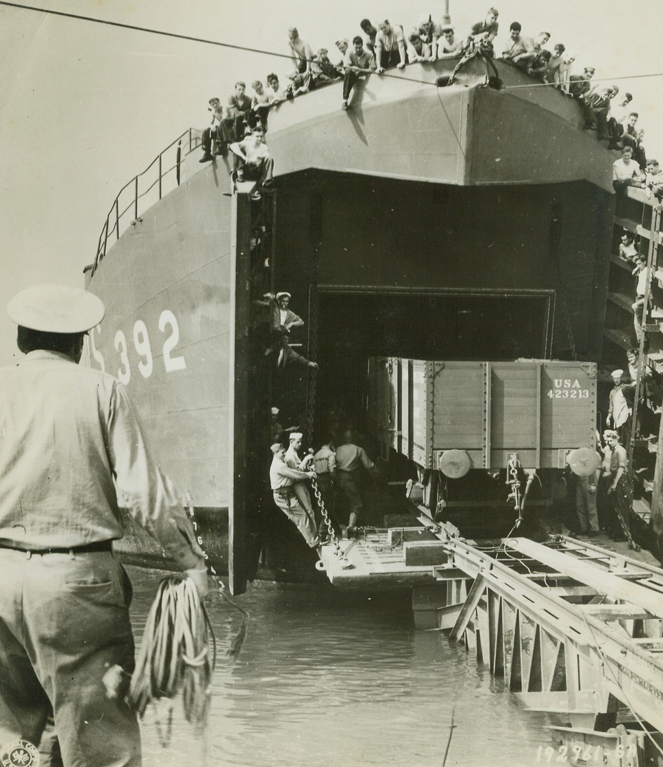 TAKE A TRAIN FROM A BOAT, 8/29/1944. FRANCE – In the first such attempt ever made, freight cars are brought ashore at Cherbourg harbor from an LST.  A specially constructed ramp made of railway tracks, facilitates the job. Credit: Signal Corps photo from Acme;