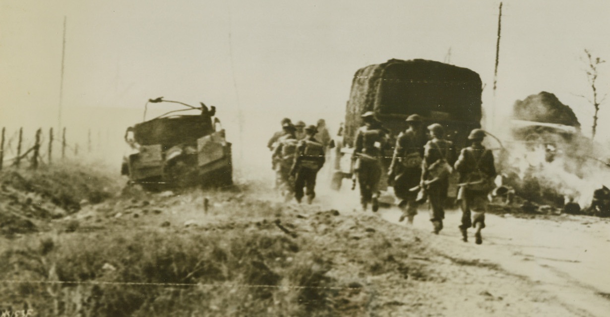 SOUTH TO FALAISE, 8/12/1944. FRANCE – Canadian infantrymen and army vehicles circle around a vehicle which has been knocked out by the side of the road, as the Canadian Army advances South on the road to Falaise. Credit: Canadian official photo via Signal Corps radio telephoto from Acme;