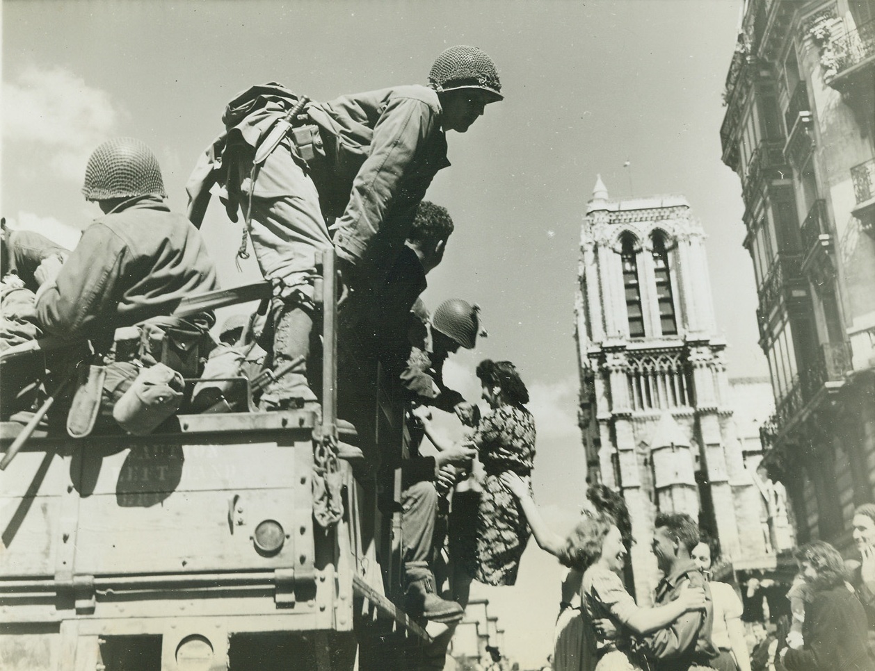 Welcome to the Liberating Americans, 8/28/1944. Paris – United States soldiers are shown being joyfully greeted by French women in the shadow of Notre Dame Cathedral. They dance – and one girl may be pulling a soldier from the truck. Credit: ACME photo by Bert Brandt for the War Picture Pool;