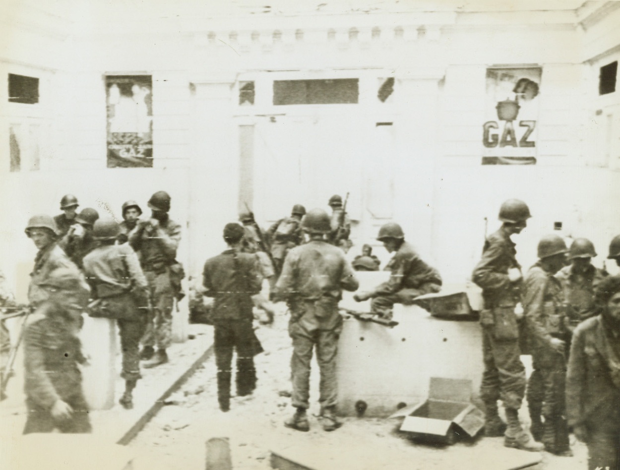 “Soup’s On” in St. Malo, 8/17/1944. France – Americans gather in an empty store in the Breton town of St. Malo for chow. In the background, German prisoners are seated on the curb. In left foreground and just to left of center are two Spanish Loyalists (former leaders) now fighting with the Yanks. Credit: Army Radiotelephoto from ACME;