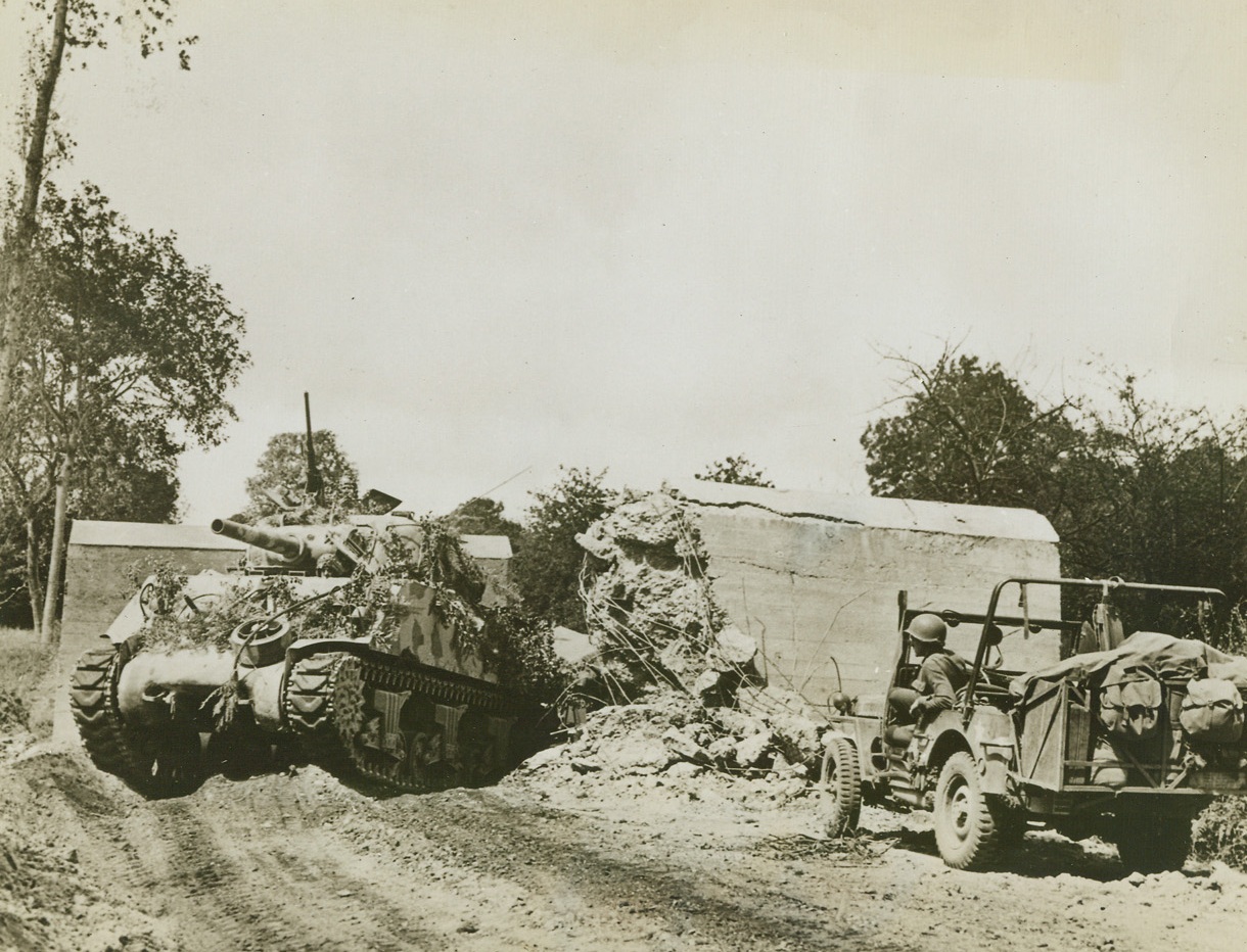 Road Block No Obstacle, 8/5/1944. France – An American tank smashes through a road block on its way to join the American lightning attack on the Avranches sector during the current offensive in Brittany. Tank is camouflaged with twigs and paint. Note how the so-called block is completely demolished. Credit: ACME;