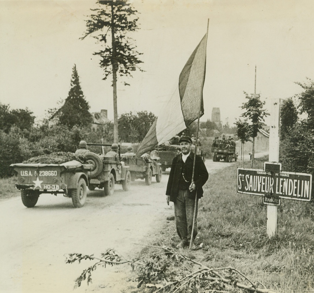 Tricolor Salute, 8/8/1944. France – An American Armored Division receives a greeting from this old French man with a Tricolor on a staff, as it rolls into St. Sauveur Lendelin. Credit: ACME;