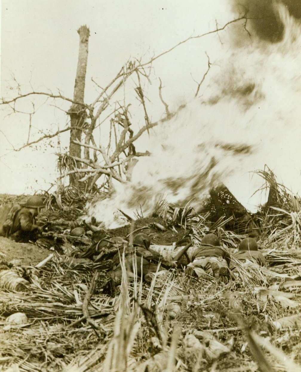 Burn Japs Out of Hiding, 8/2/1944. Guam-- While a Marine (Left) uses a flame thrower to burn the enemy out of a hidden pillbox on Guam, his buddies wait with guns poised for the Japs to show themselves. Although surrounded by leathernecks, the Japs refused to Surrender. (ACME);