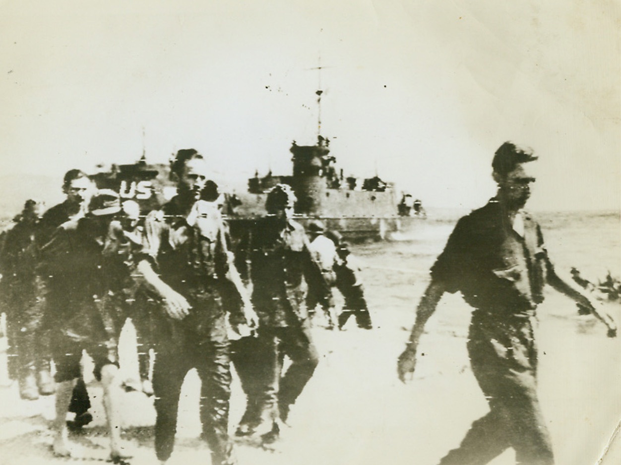 First Prisoners in New Invasion, 8/16/1944. France – As Allied troops come ashore from the LCIs in background, a group of Germans—first prisoners taken in the invasion of Southern France—march along the beach under guard. Credit: Army Radiotelephoto from ACME;