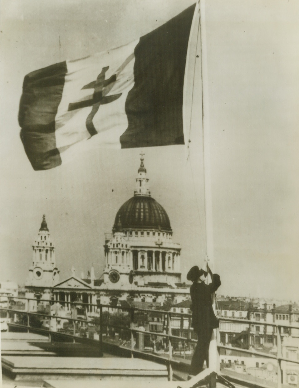 Marking Liberation of Paris, 8/23/1944. London – By way of celebration of the Liberation of Paris, Londoners hoisted a flag bearing the Cross of Lorraine to wave over the British capital. In the background is St. Paul’s Cathedral. Credit: ACME Radiophoto;