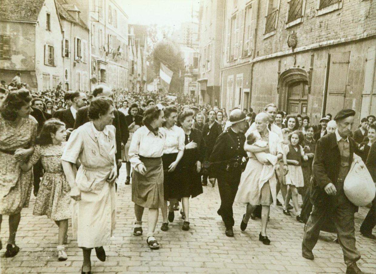 Collaborationist Is Scorned By Her People, 8/26/1944. Chartres, France -- Followed by jeering townspeople, a woman collaborator is led back to her home after having her hair shaved off. The shorn woman carries a German baby. The French Tricolour (Background) flies from the middle of the street and American flags are hung out of windows as French people celebrate the liberation of Chartres by the Yanks. 8/26/44 (ACME);