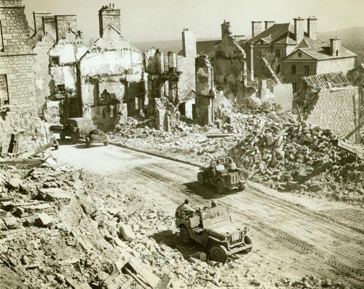 Past The Ruins To Paris, 8/21/1944. France – The crumbled ruins of buildings wrecked by bombs and shells line the sides of the road to Paris. American vehicles move up past this battered town, forging ahead to support the Third Army’s lighting advance on the French capital. 8/21/44 (ACME Photo By Bert Brand For The War Picture Pool);