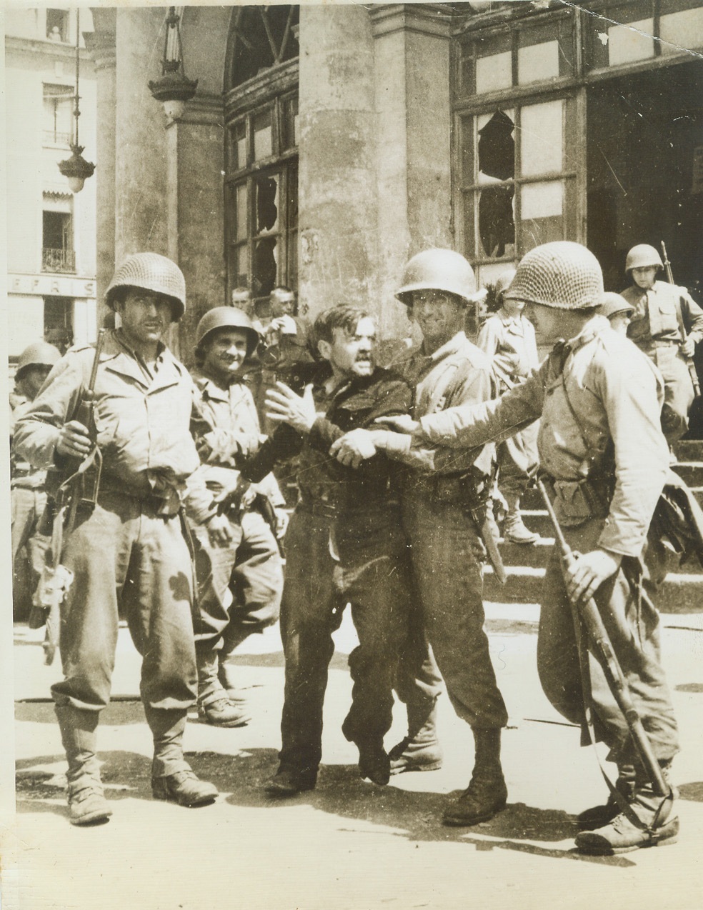 Underdog Turns on Nazis, 8/11/1944. Rennes, France—While American soldiers restrain him, this French patriot struggles to free himself and vent his wrath on disarmed Nazi prisoners of war gathered on the Rennes City Hall steps. Finally freed of Nazi oppression, he fought to get at those who were responsible for the tyrannical treatment.  Credit: ACME;